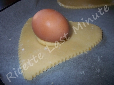 Impasto steso e tagliato a forma di cuore con uovo sodo applicato al di sopra